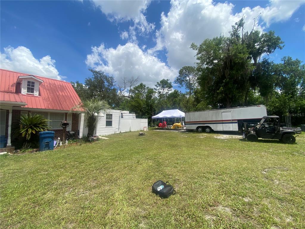 A grassy backyard features a house with a red roof, a trailer, and a canopy — 219 SHADY LANE, ORANGE CITY, FL