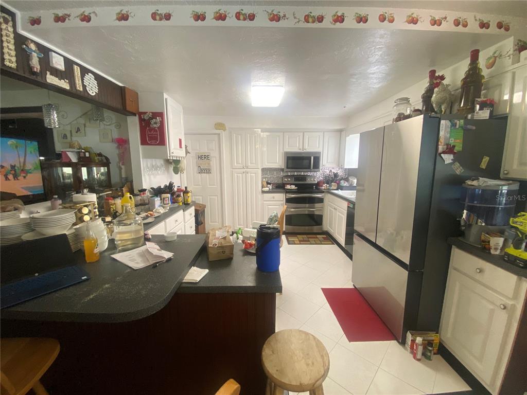 A kitchen features white cabinetry, stainless steel appliances, a dark countertop, and tiled flooring — 219 SHADY LANE, ORANGE CITY, FL