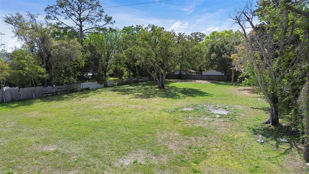 A large, grassy, vacant residential lot features several mature trees and a wooden perimeter fence — 11602 IROQUOIS TRAIL, ORLANDO, FL