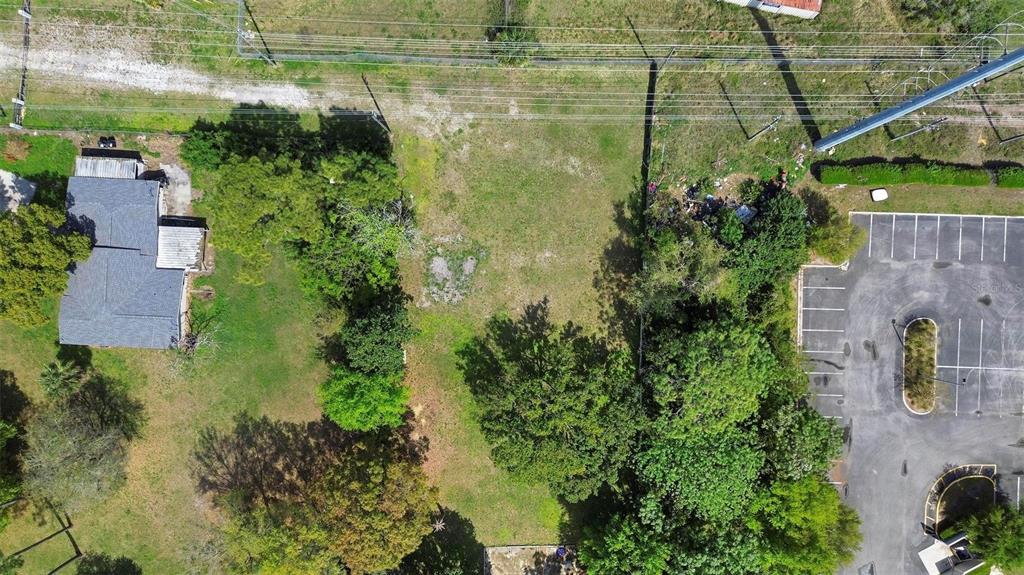 An aerial view shows a vacant, grassy lot situated between a residential house and a parking lot — 11602 IROQUOIS TRAIL, ORLANDO, FL