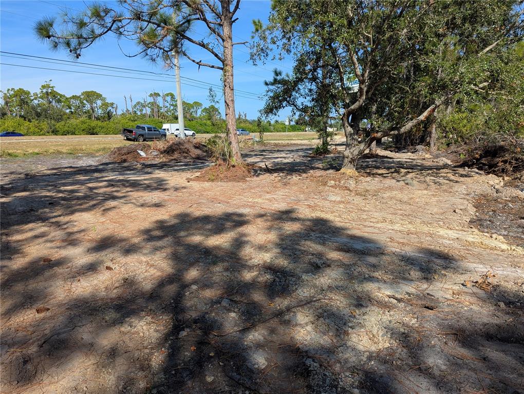 A cleared, sandy lot features two large trees and a road with vehicles in the background — 3512 EL JOBEAN ROAD, PORT CHARLOTTE, FL