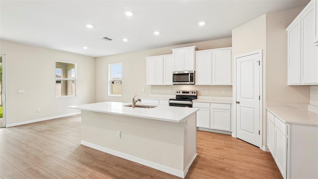 A modern kitchen features white cabinets, a central island with a sink, and wood-look flooring — 18209 GANDER TERRACE, LAKEWOOD RANCH, FL