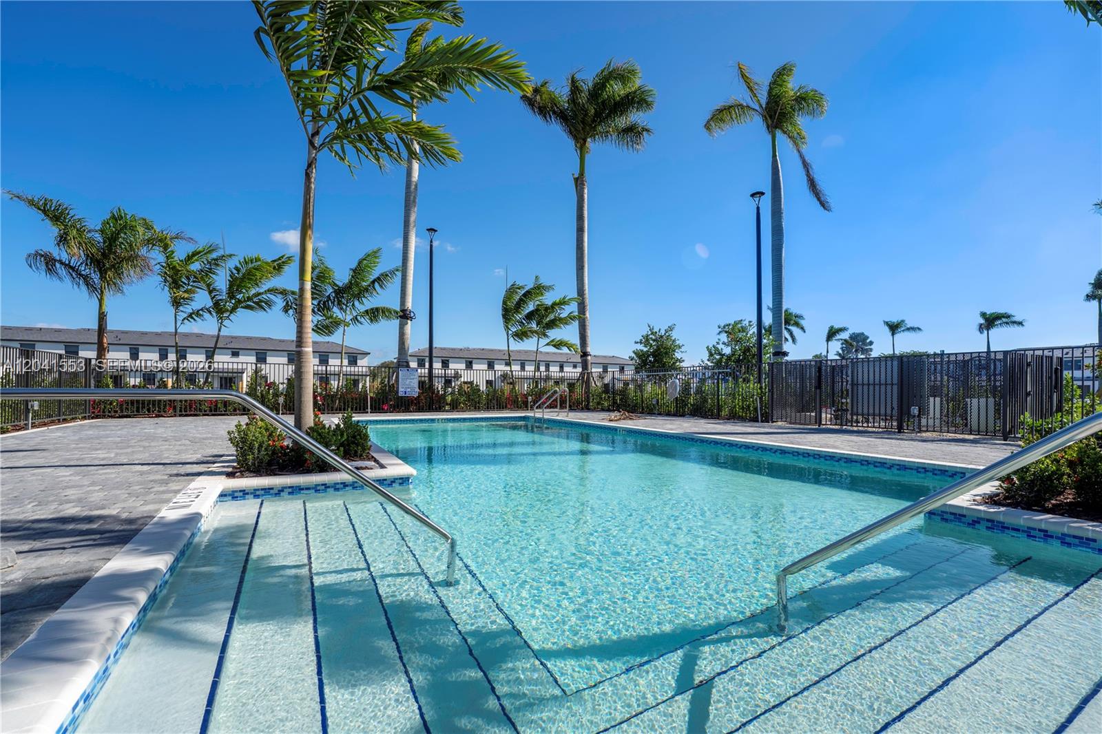 An outdoor swimming pool with steps and metal handrails surrounded by palm trees and fencing — 5001 Peacock Way # 5838, Dania Beach FL 33312, DANIA BEACH, FL