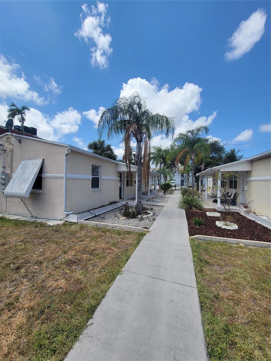 A concrete walkway leads between two single-story buildings with palm trees and landscaping — 1822 Johnson Street, Hollywood FL 33020, HOLLYWOOD, FL