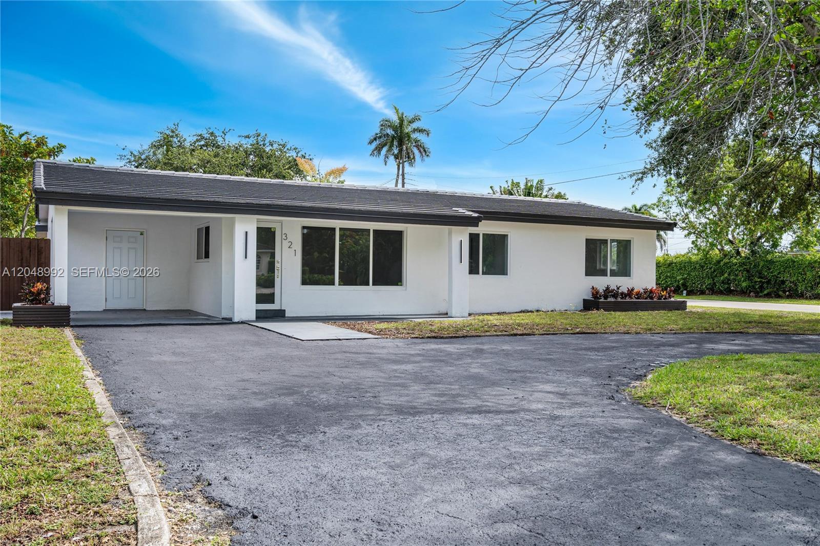 A single-story white house with a dark roof and a paved driveway sits under a blue sky — 321 NW 36th St, Oakland Park FL 33309, OAKLAND PARK, FL