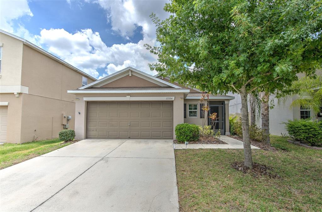 A single-story house with a tan stucco exterior, a two-car garage, and a front tree — 17334 WHITE MANGROVE DRIVE, WIMAUMA, FL