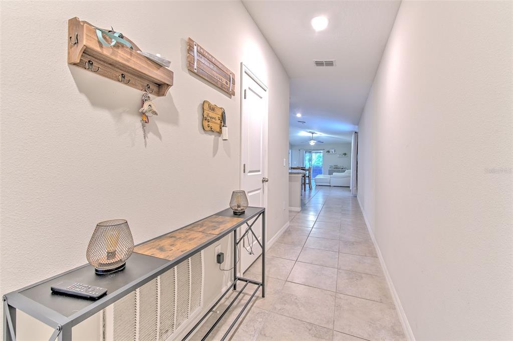 A hallway with tile flooring leads from a console table toward an open living area — 17334 WHITE MANGROVE DRIVE, WIMAUMA, FL