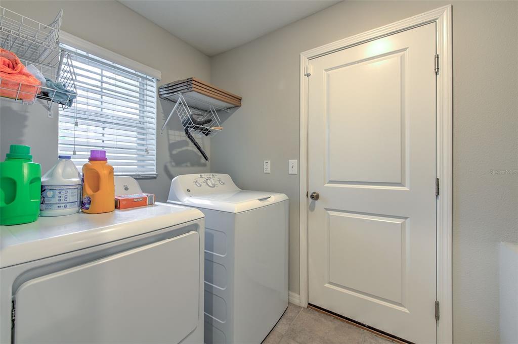 A laundry room features a white washer and dryer, shelving, and a white door — 17334 WHITE MANGROVE DRIVE, WIMAUMA, FL