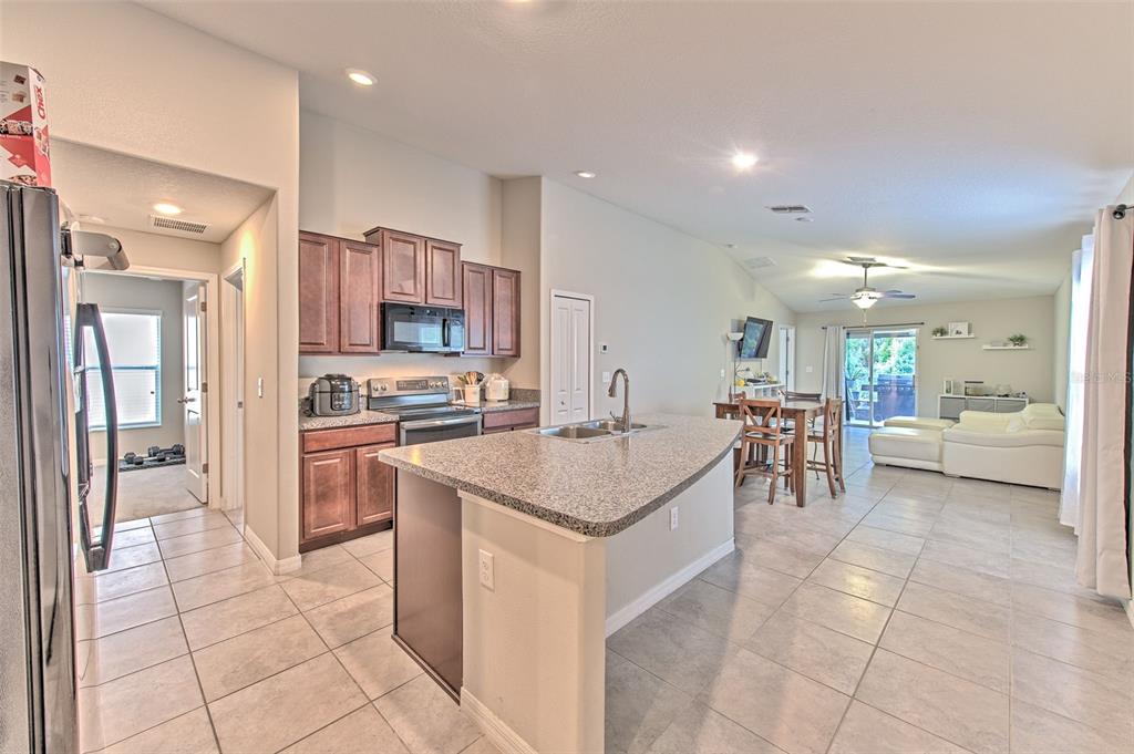 A kitchen with granite countertops and dark wood cabinets opens into a dining and living area — 17334 WHITE MANGROVE DRIVE, WIMAUMA, FL