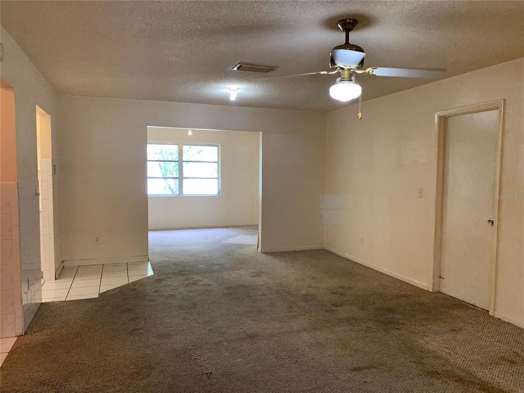 A living room with beige carpet, a ceiling fan, and an adjacent tiled entryway — 9598 RIVER ROAD, SPRING HILL, FL