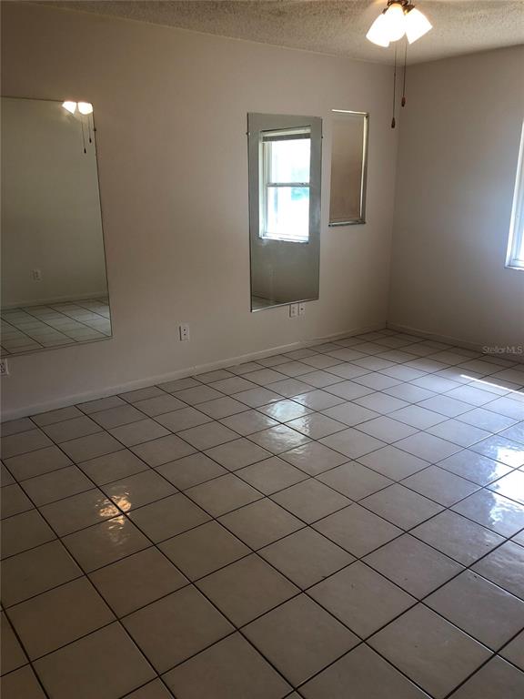 An empty room features white tile flooring, two wall-mounted mirrors, and a ceiling light fixture — 9598 RIVER ROAD, SPRING HILL, FL