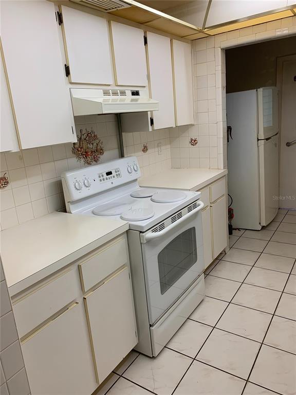 A kitchen features white cabinets, a white electric range, and light-colored tiled floors and walls — 9598 RIVER ROAD, SPRING HILL, FL