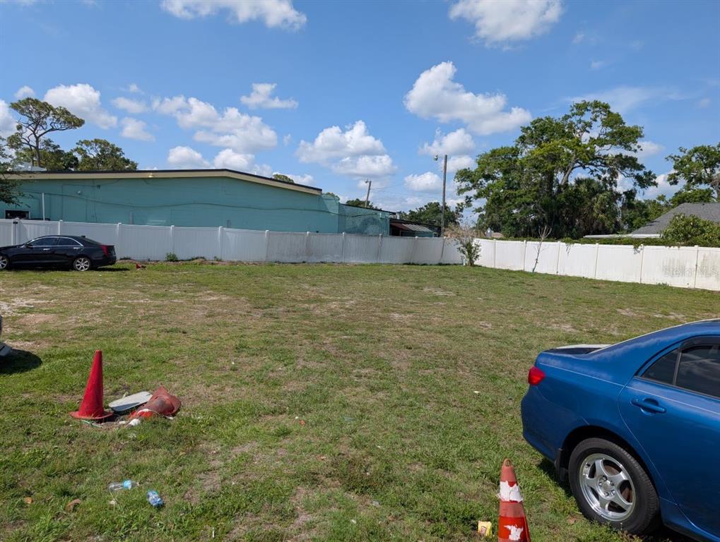 A vacant, grassy lot is enclosed by a white vinyl fence under a blue sky — 7019 N MANHATTAN AVENUE, TAMPA, FL