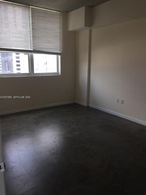 A kitchen with white cabinets and stainless steel appliances sits in an open concrete-floored room — 133 NE 2nd Ave # 913, Miami FL 33132, MIAMI, FL