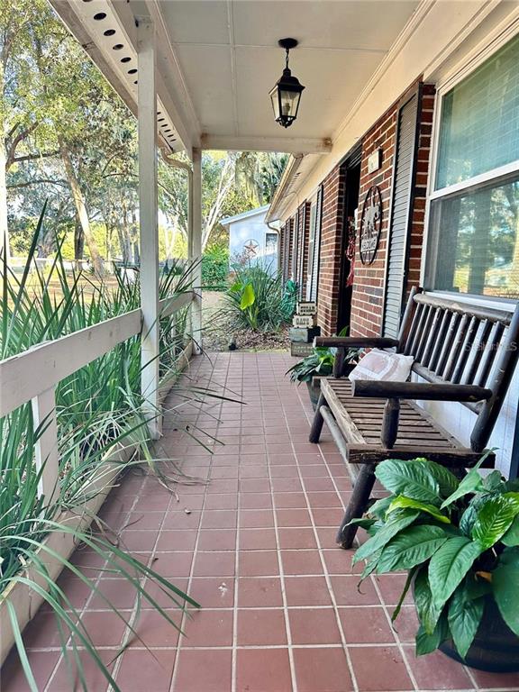 A covered brick porch features a wooden bench, a hanging lantern, and potted plants — 13565 NE 38TH AVENUE, ANTHONY, FL
