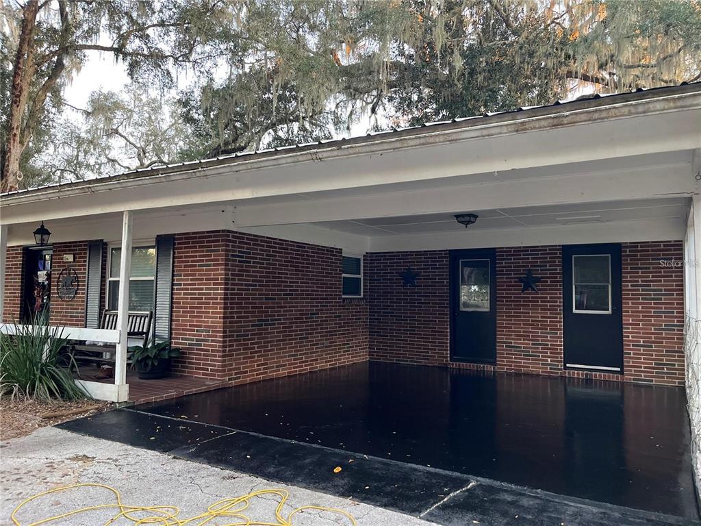 A brick house exterior features a covered carport with a dark painted concrete floor — 13565 NE 38TH AVENUE, ANTHONY, FL