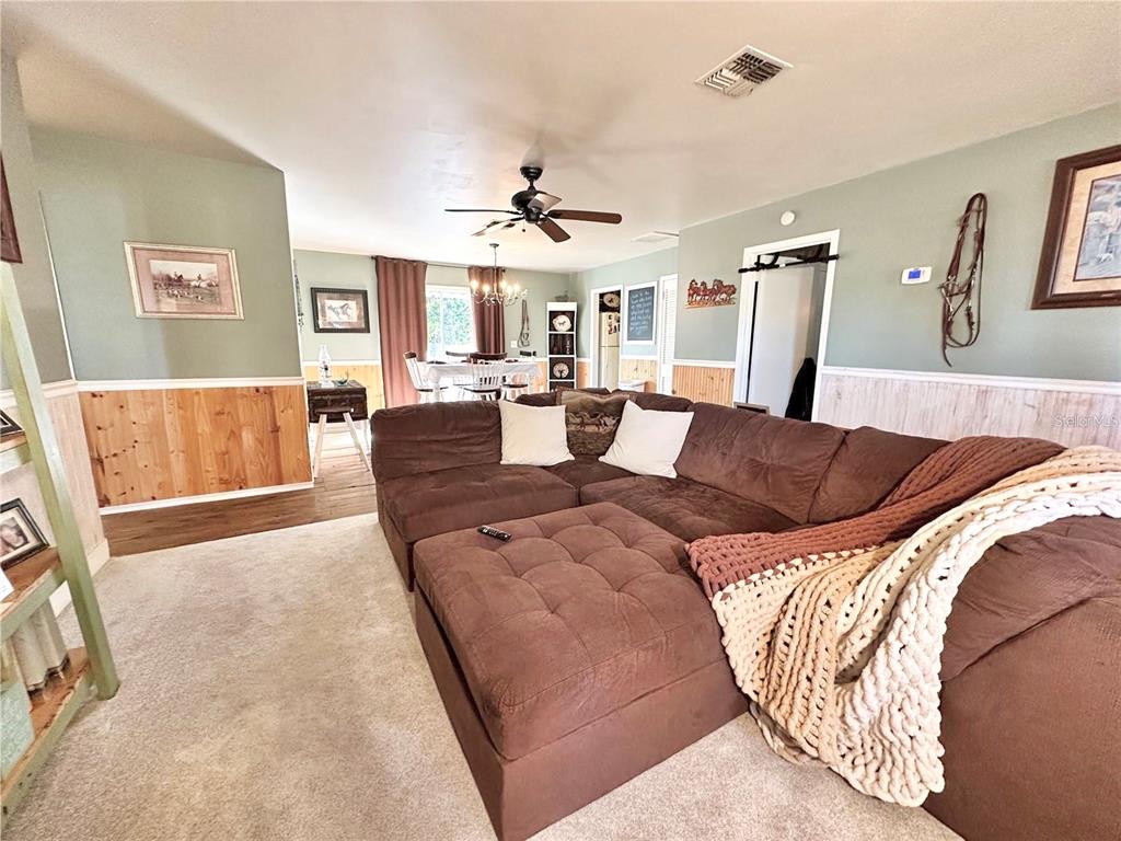 A living room features a large brown sectional sofa, carpeted floors, and wood wainscoting — 13565 NE 38TH AVENUE, ANTHONY, FL