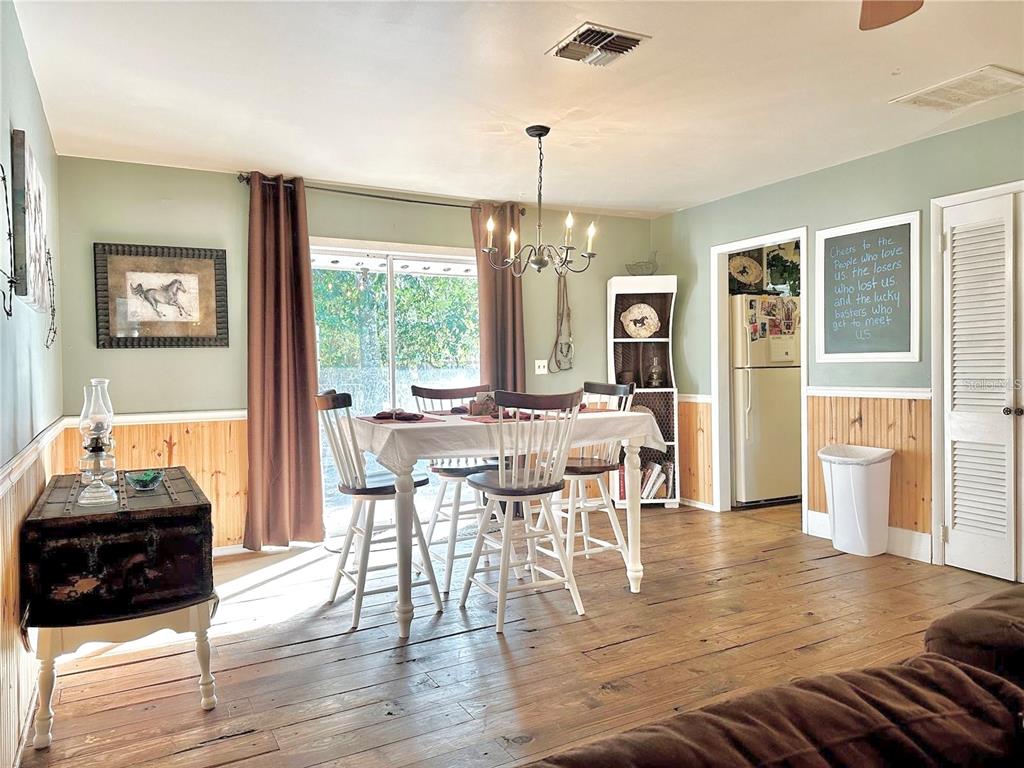 A dining room features wood floors, wainscoting, a chandelier, and a sliding glass door — 13565 NE 38TH AVENUE, ANTHONY, FL