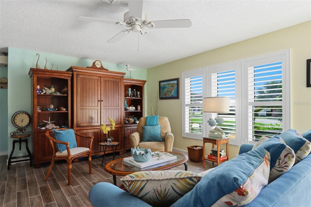 A living room features a large wooden entertainment center, blue furniture, and white plantation shutters — 510 CIRCLEWOOD DRIVE UNIT P1-2, VENICE, FL