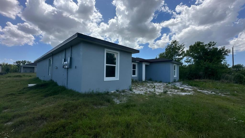 A blue-painted house exterior with white-trimmed windows stands on a grassy, undeveloped lot — 12223 KIRK AVENUE, PORT CHARLOTTE, FL