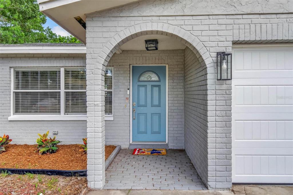 A light blue front door is set within a brick archway under a covered porch — 3113 PALM COURT, DUNEDIN, FL