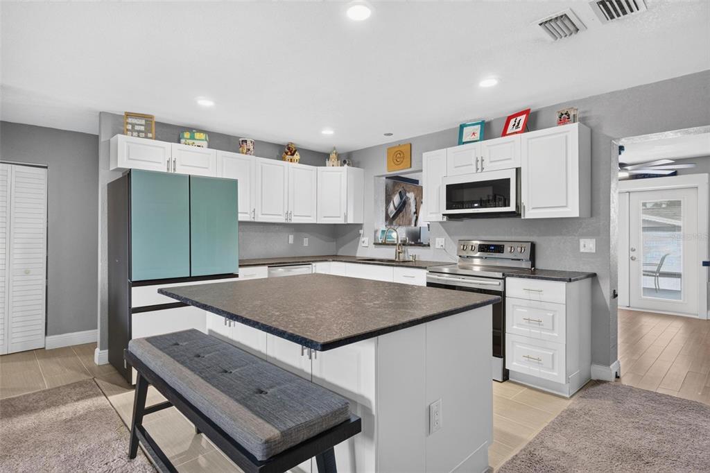 A kitchen features white cabinets, a dark countertop island with a bench, and stainless appliances — 3113 PALM COURT, DUNEDIN, FL