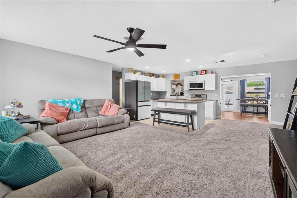 A living room with gray carpet opens to a kitchen featuring white cabinets and island — 3113 PALM COURT, DUNEDIN, FL