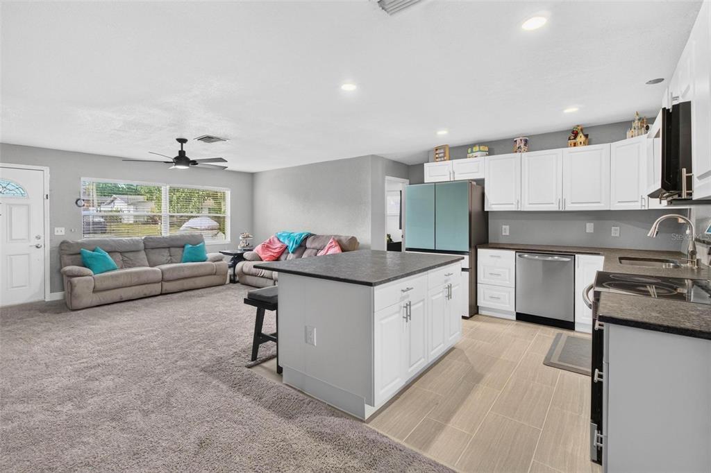 An open-concept living room and kitchen featuring gray carpet, tile flooring, and white cabinetry — 3113 PALM COURT, DUNEDIN, FL