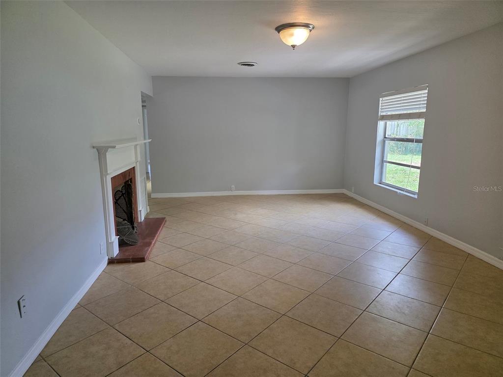 An empty living room with light gray walls, tile flooring, and a white fireplace — 1695 E HORATIO AVENUE, MAITLAND, FL