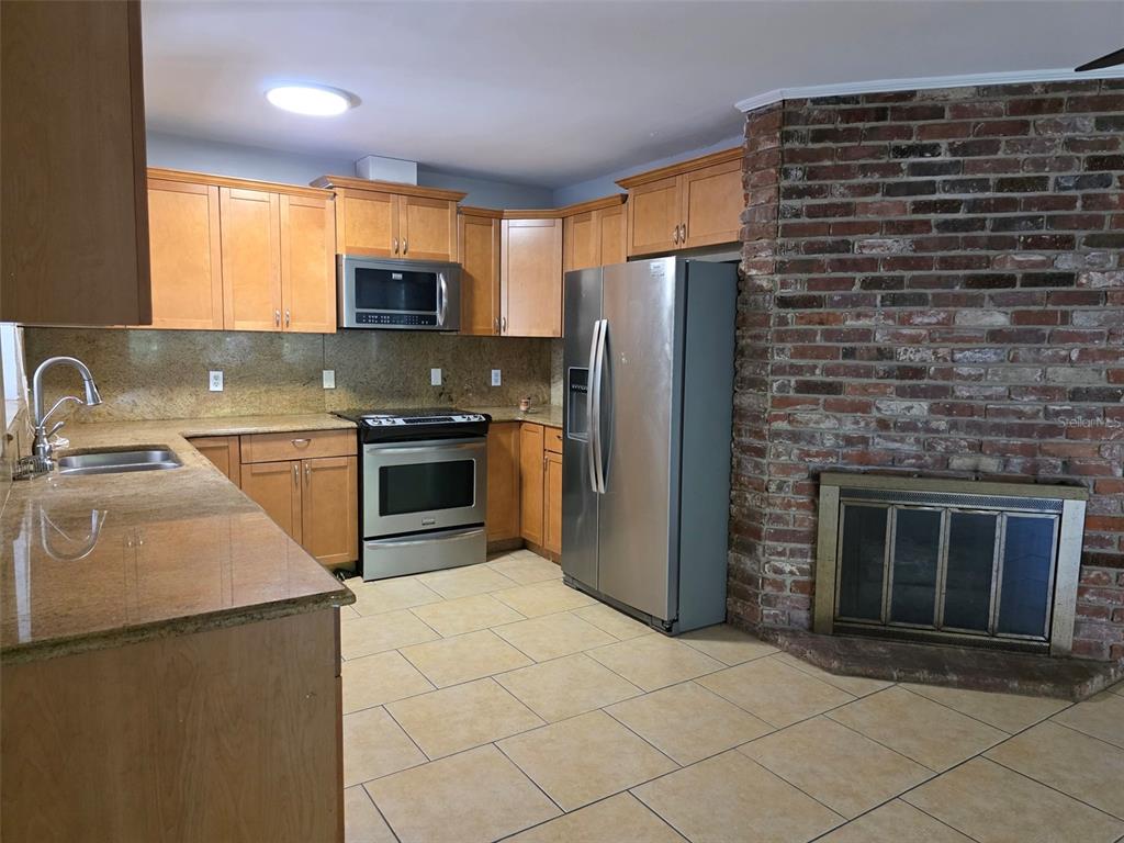A kitchen features light wood cabinets, granite countertops, stainless steel appliances, and a brick fireplace — 1695 E HORATIO AVENUE, MAITLAND, FL