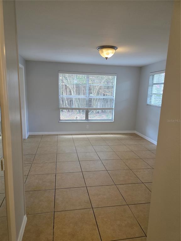 An empty room with light gray walls, large windows with blinds, and tan tile flooring — 1695 E HORATIO AVENUE, MAITLAND, FL