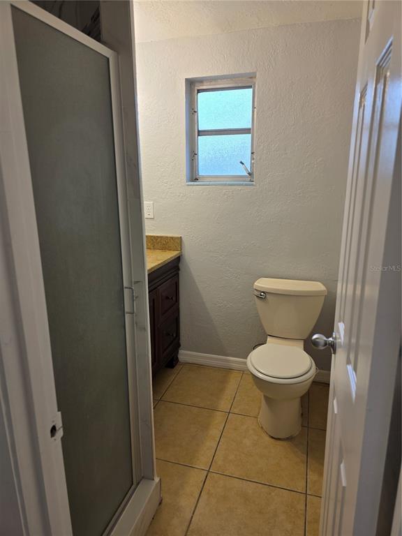 A small bathroom features a walk-in shower, a dark wood vanity, and a beige toilet — 1695 E HORATIO AVENUE, MAITLAND, FL