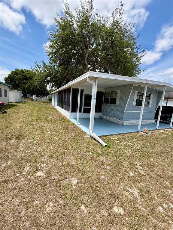 A light blue mobile home features a large attached carport and a screened-in porch area — 4513 AUTUMN PALM DRIVE, ZEPHYRHILLS, FL