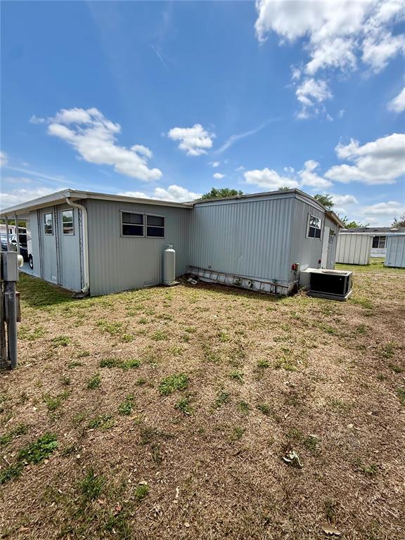 The exterior of a light gray mobile home features a propane tank and air conditioner — 4513 AUTUMN PALM DRIVE, ZEPHYRHILLS, FL