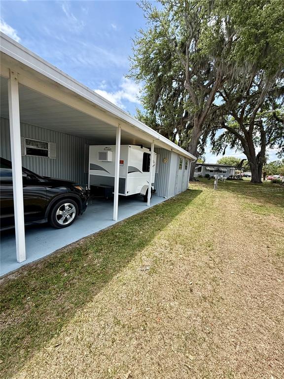 A carport shelters a black SUV and a small white travel trailer beside a house — 4513 AUTUMN PALM DRIVE, ZEPHYRHILLS, FL