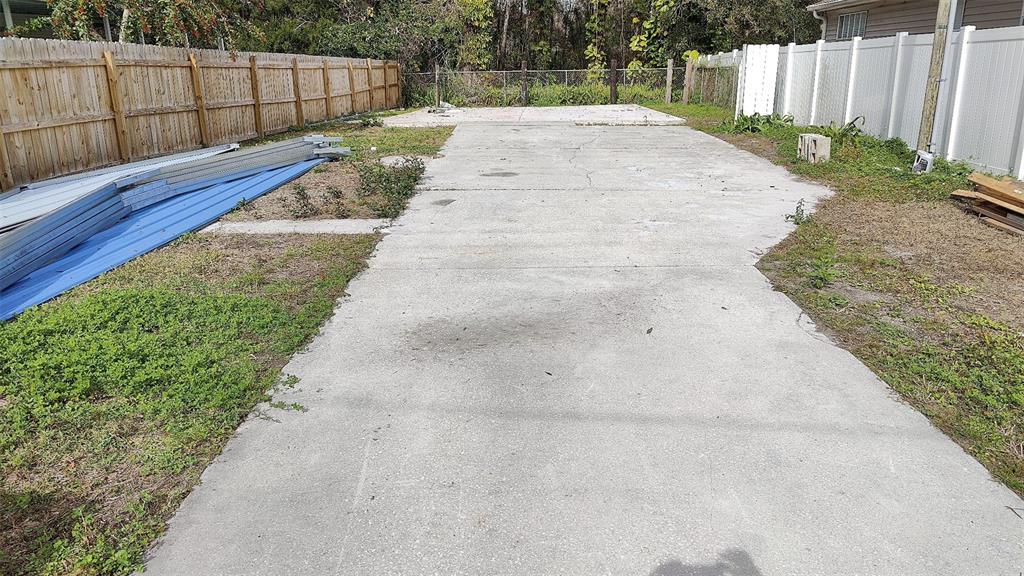 A concrete slab sits in a backyard enclosed by wooden and white vinyl privacy fences — 7717 AMHERST STREET, TAMPA, FL