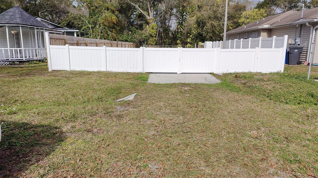 A white vinyl fence with a double gate stands in a grassy backyard — 7717 AMHERST STREET, TAMPA, FL