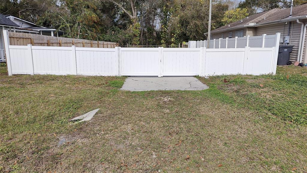 A white vinyl fence with a double gate stands in a grassy backyard — 7717 AMHERST STREET, TAMPA, FL