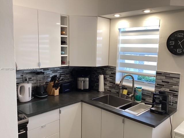 A modern kitchen features white cabinets, dark countertops, a tiled backsplash, and a window — 3133 S Ocean Dr # 118, Hallandale Beach FL 33009, HALLANDALE BEACH, FL