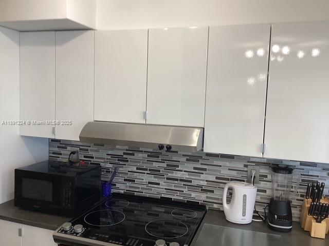 A kitchen features white glossy cabinets, a stainless steel range hood, and a tiled backsplash — 3133 S Ocean Dr # 118, Hallandale Beach FL 33009, HALLANDALE BEACH, FL