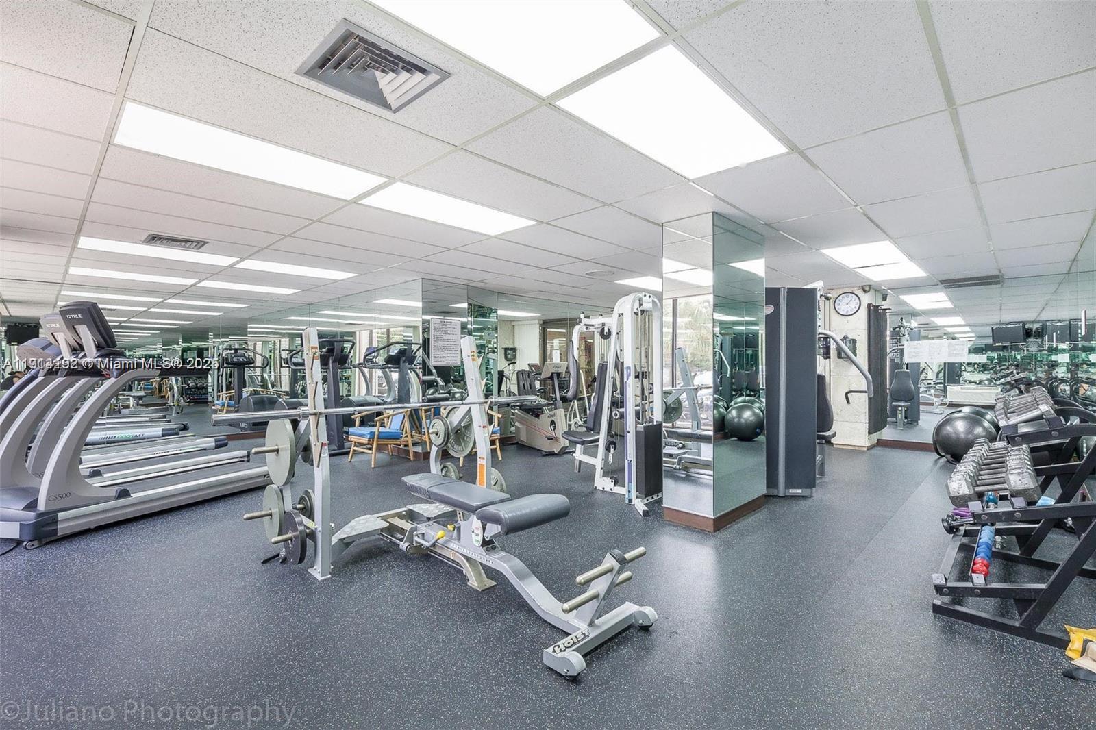 A gym features treadmills, weight machines, free weights, and mirrored walls under a drop ceiling — 1965 S Ocean Dr # M, Hallandale Beach FL 33009, HALLANDALE BEACH, FL
