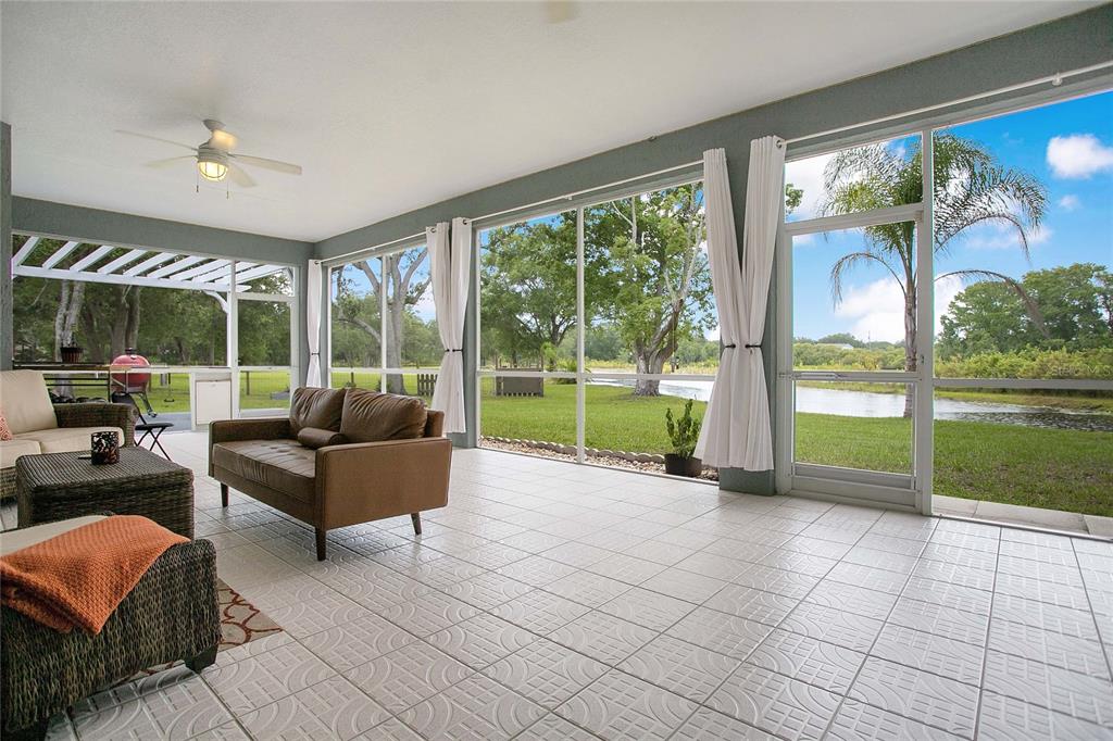 A screened-in porch with tile flooring overlooks a grassy yard and a pond — 19616 LIVINGSTON AVENUE, LUTZ, FL