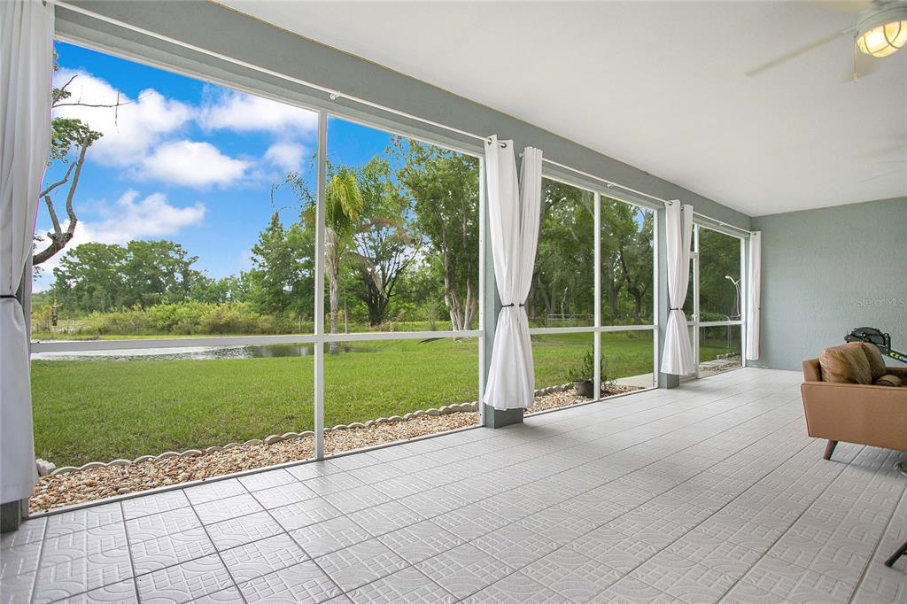A screened-in patio with tiled flooring overlooks a grassy yard and a small pond — 19616 LIVINGSTON AVENUE, LUTZ, FL