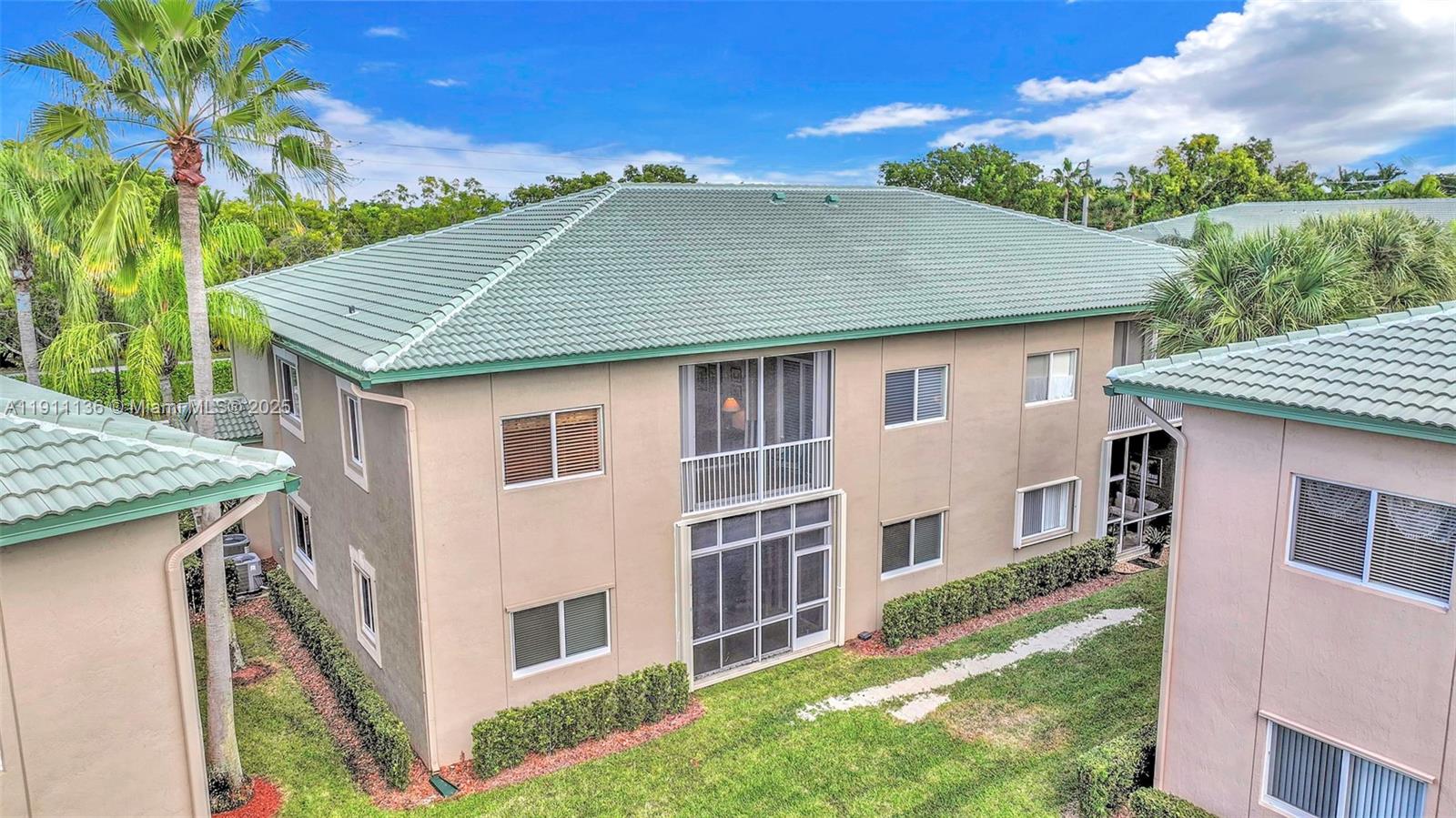 An exterior view of a two-story tan building with a green tiled hip roof — 7921 E Exeter Blvd E # 202, Tamarac FL 33321, TAMARAC, FL