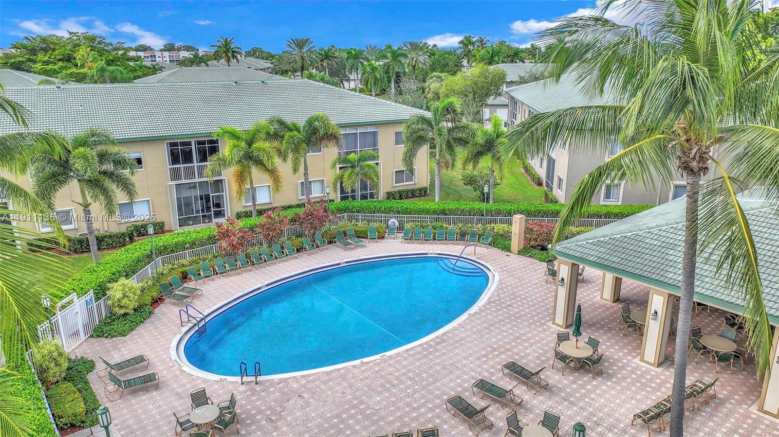 An elevated view of an outdoor swimming pool surrounded by lounge chairs and palm trees — 7921 E Exeter Blvd E # 202, Tamarac FL 33321, TAMARAC, FL