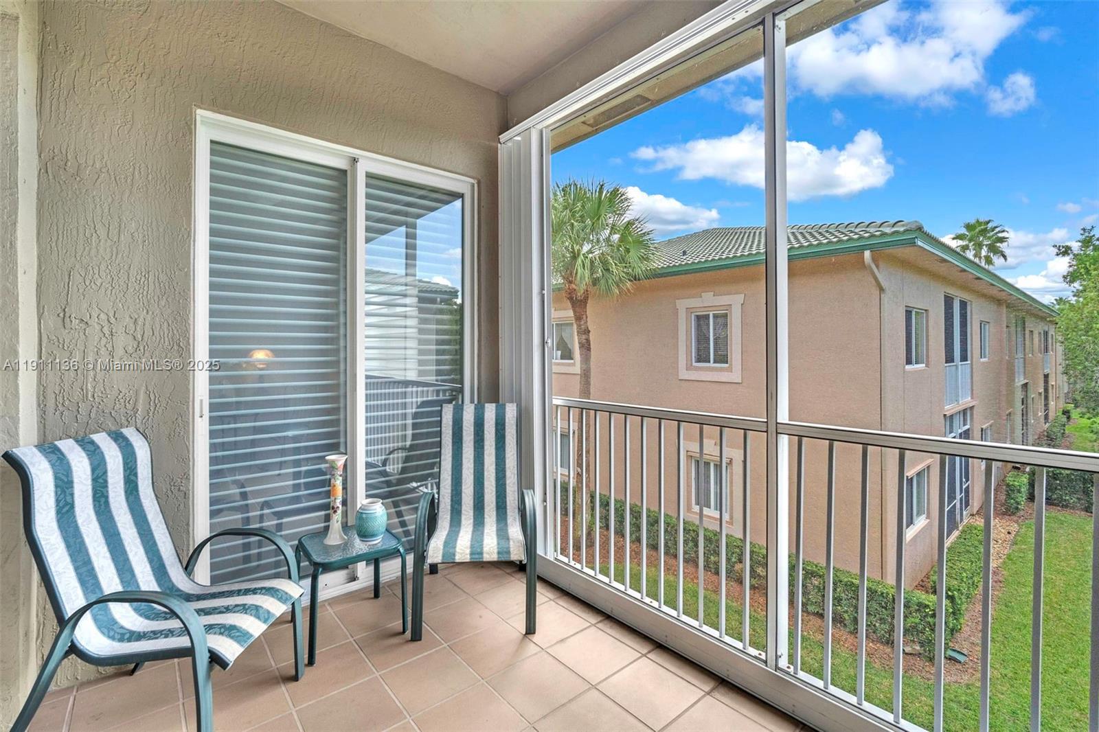 A screened-in balcony features tiled flooring, two striped chairs, a small table, and exterior views — 7921 E Exeter Blvd E # 202, Tamarac FL 33321, TAMARAC, FL