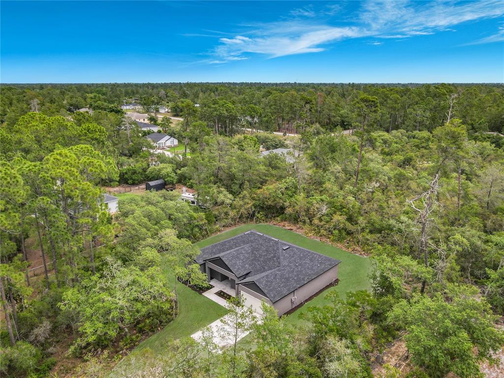 An aerial view shows a single-story house with a dark roof surrounded by dense forest — 41260 BALSAM STREET, EUSTIS, FL