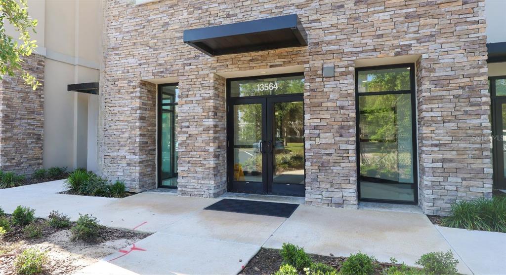 The exterior of a commercial building features a stone facade, glass double doors, and awnings — 13564 VILLAGE PARK DRIVE UNIT O-365, ORLANDO, FL