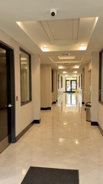 A long, brightly lit hallway with light-colored tile floors and a dark door on the left — 13564 VILLAGE PARK DRIVE UNIT O-365, ORLANDO, FL