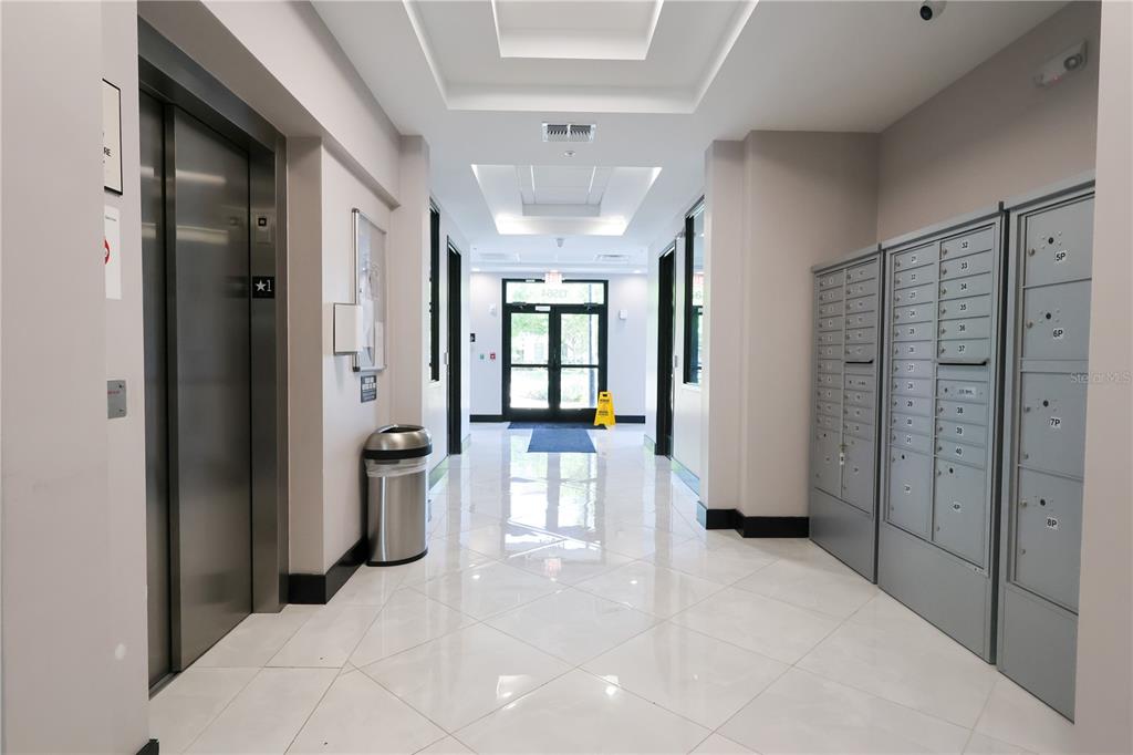 A bright apartment building lobby features a stainless steel elevator, mailboxes, and glass entry doors — 13564 VILLAGE PARK DRIVE UNIT O-365, ORLANDO, FL